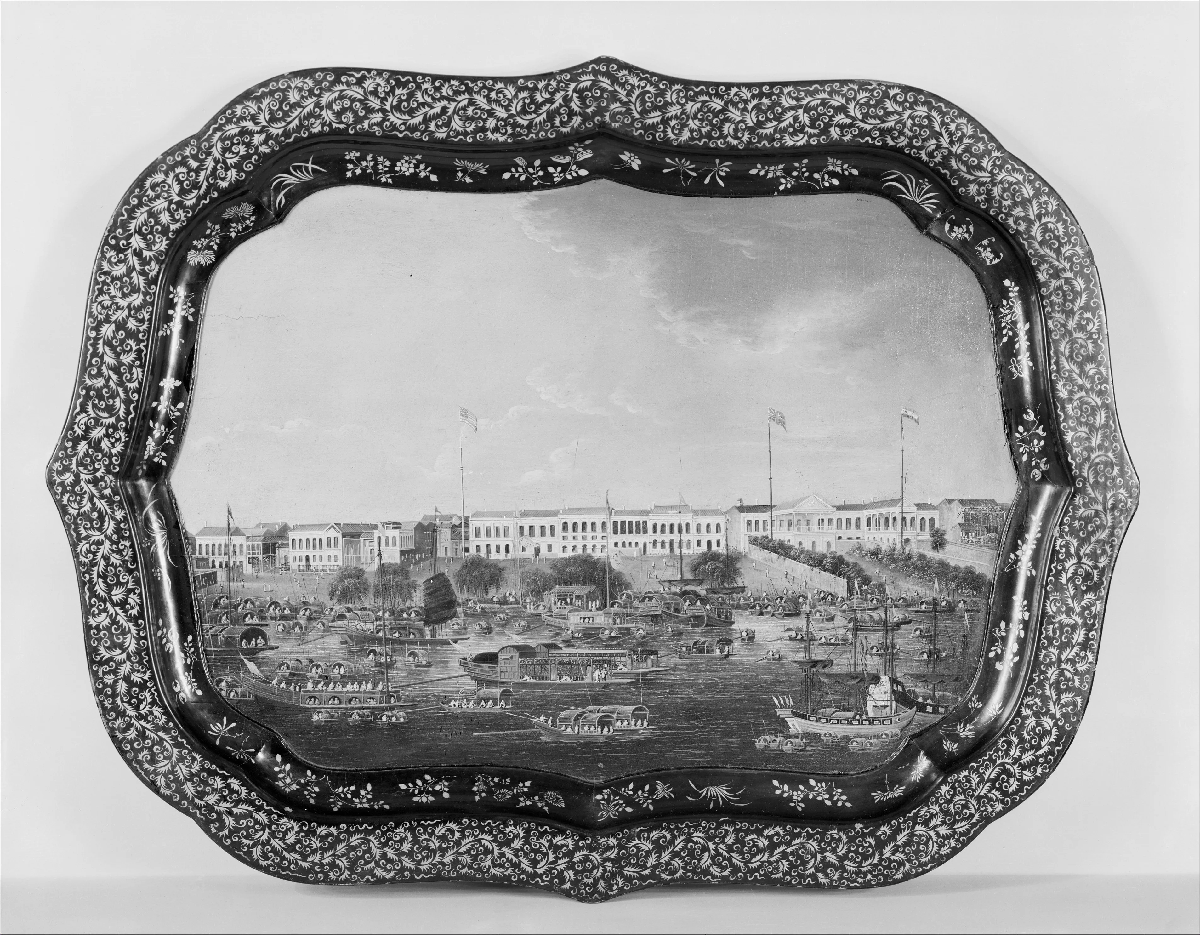 A rectangular black lacquer tray decorated with a panoramic view of the Canton waterfront, including rows of foreign factories, national flags, boats, and figures.