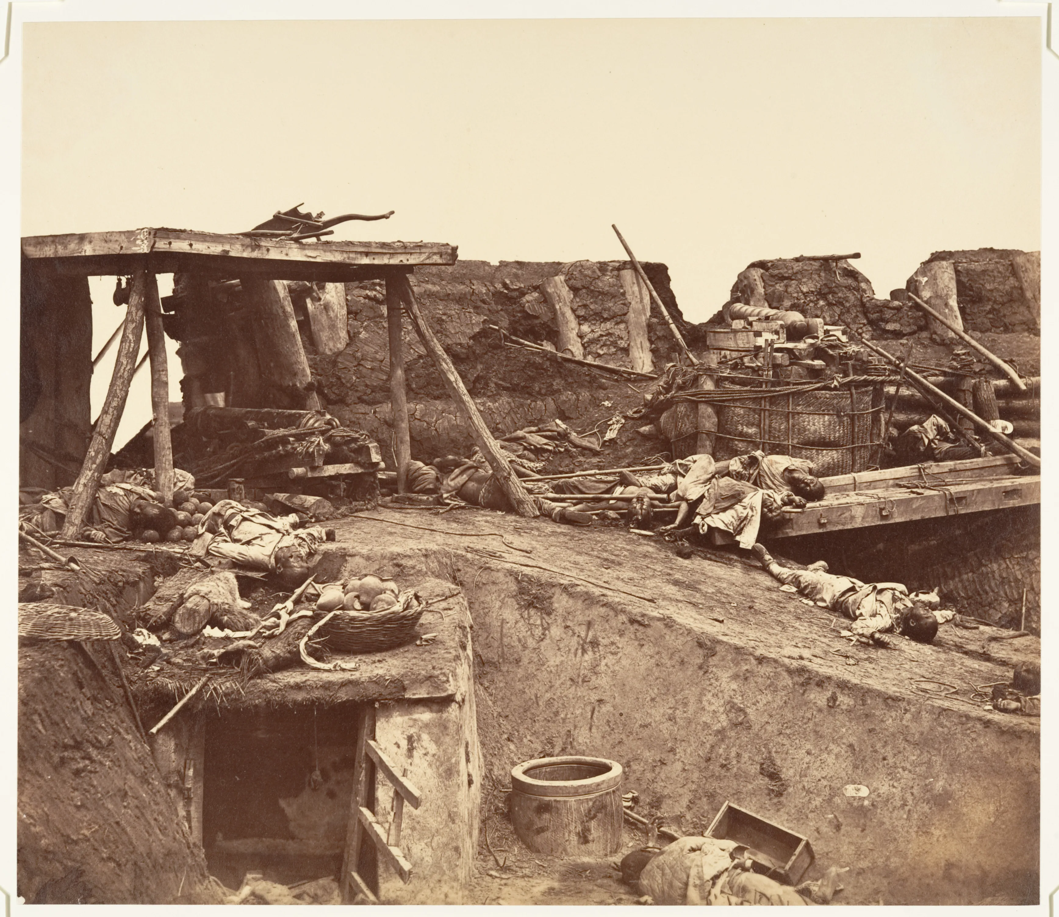 A sepia photograph shows a shattered earthen fortification after battle, with broken structures, scattered equipment, and the bodies of Chinese defenders across the ground.