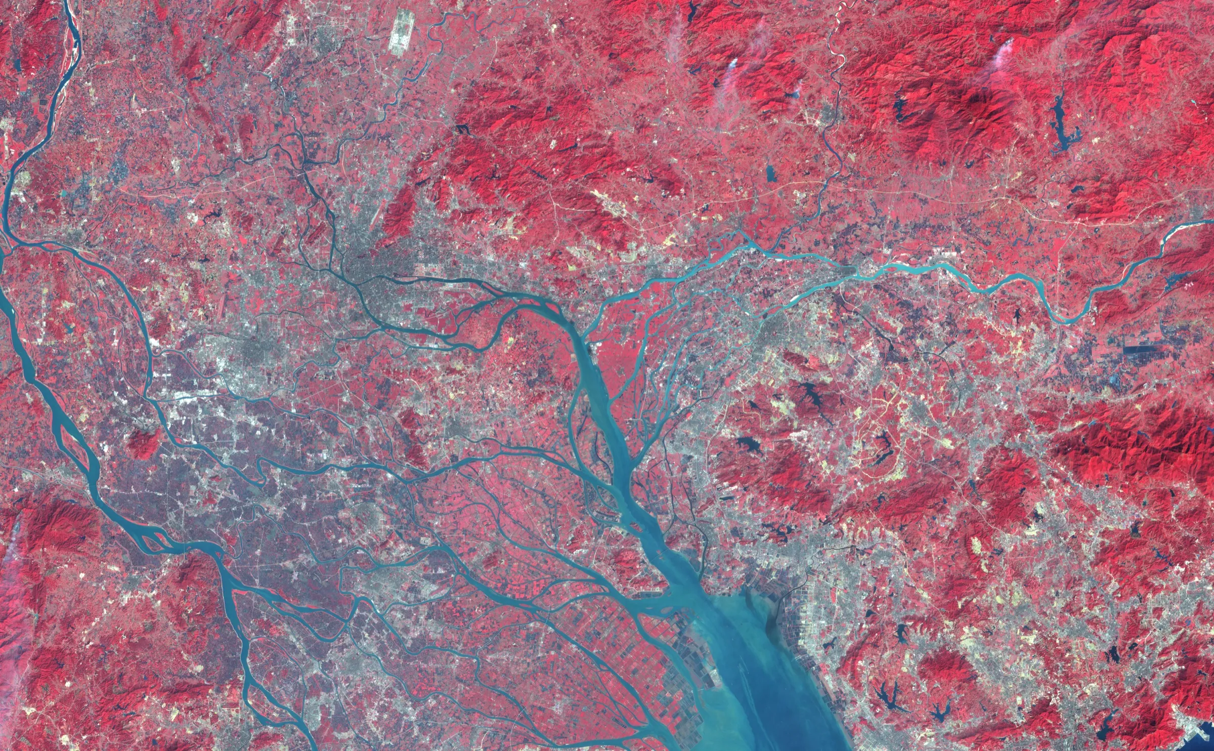 A false-colour satellite image of the Pearl River Delta in 2003, with extensive grey urban surfaces spreading around blue-green waterways and between red hills.