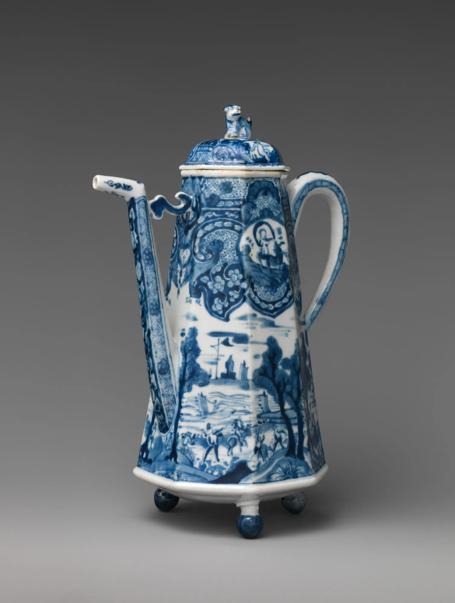A tall blue-and-white porcelain coffeepot with an angular spout, loop handle, animal finial, patterned panels, and small landscape scenes.