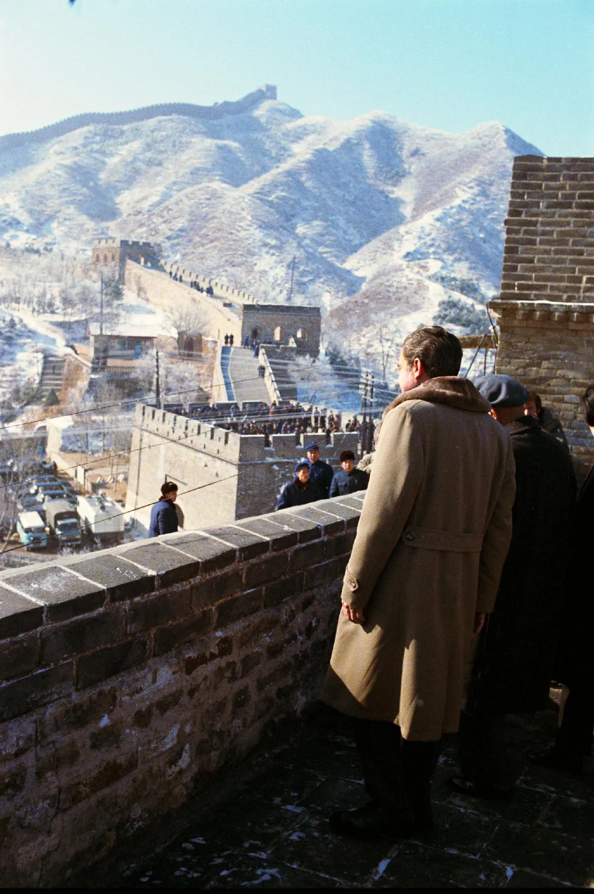 Seen from behind, Richard Nixon stands on the snow-dusted Great Wall at Badaling and looks toward watchtowers climbing through the mountains.