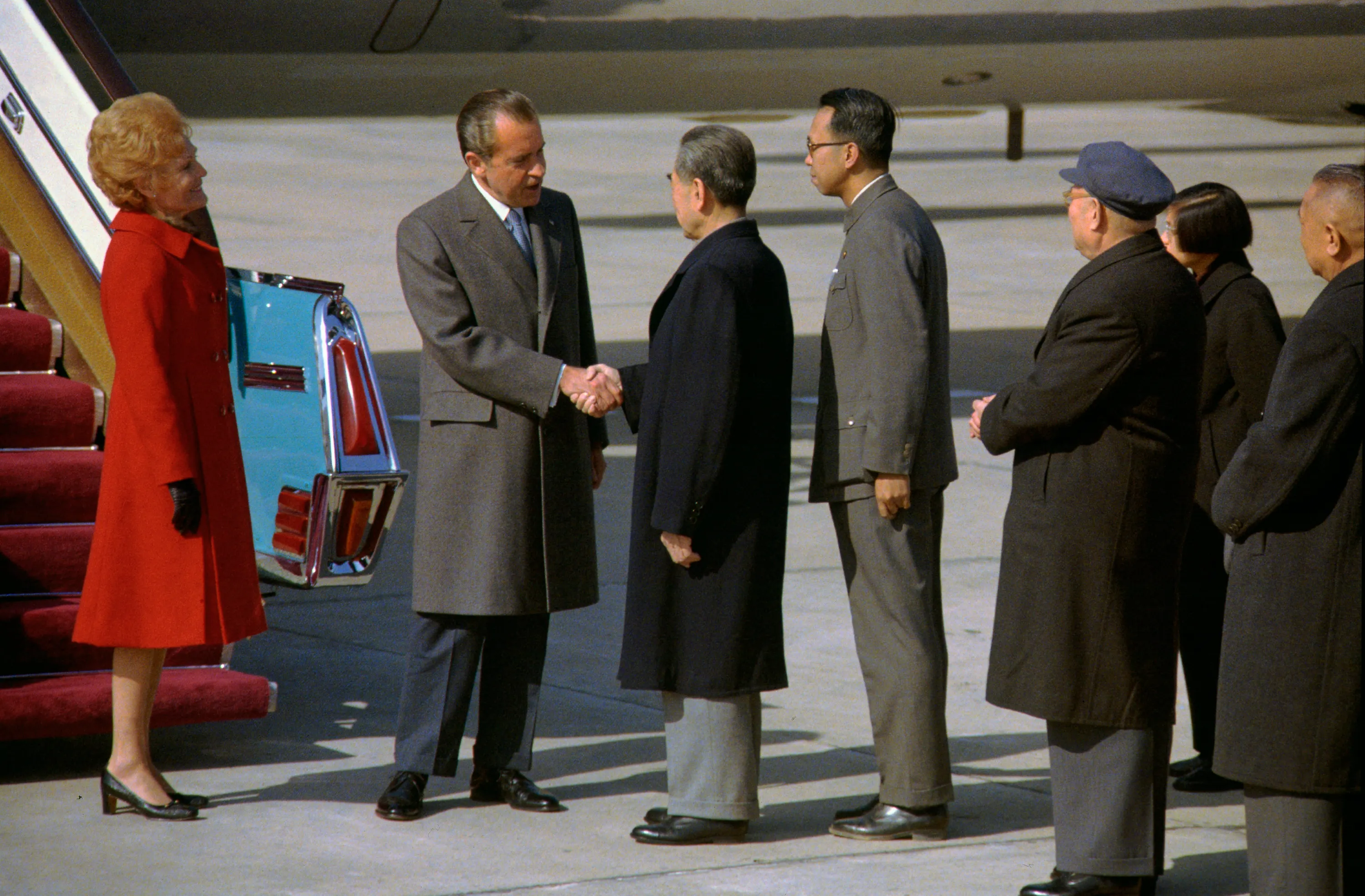 Richard Nixon shakes Zhou Enlai’s hand beside Air Force One while Pat Nixon and a line of Chinese officials watch on the Beijing airport apron.