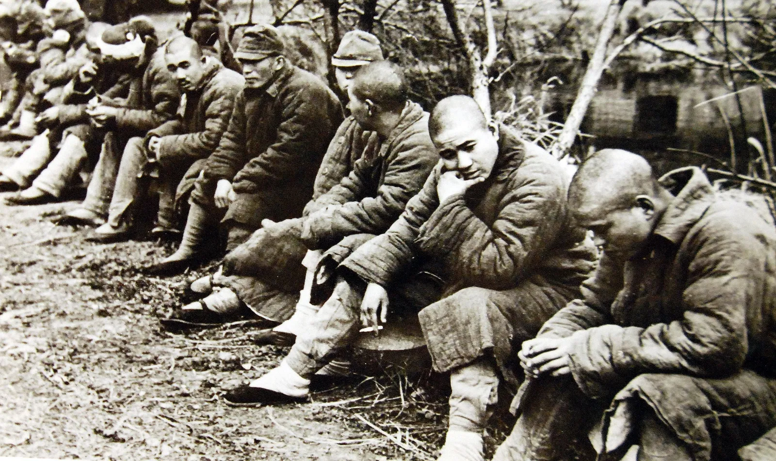 A row of captured Japanese soldiers in padded winter uniforms sits on the ground after the Battle of Changsha, several looking toward the camera while others bow their heads.