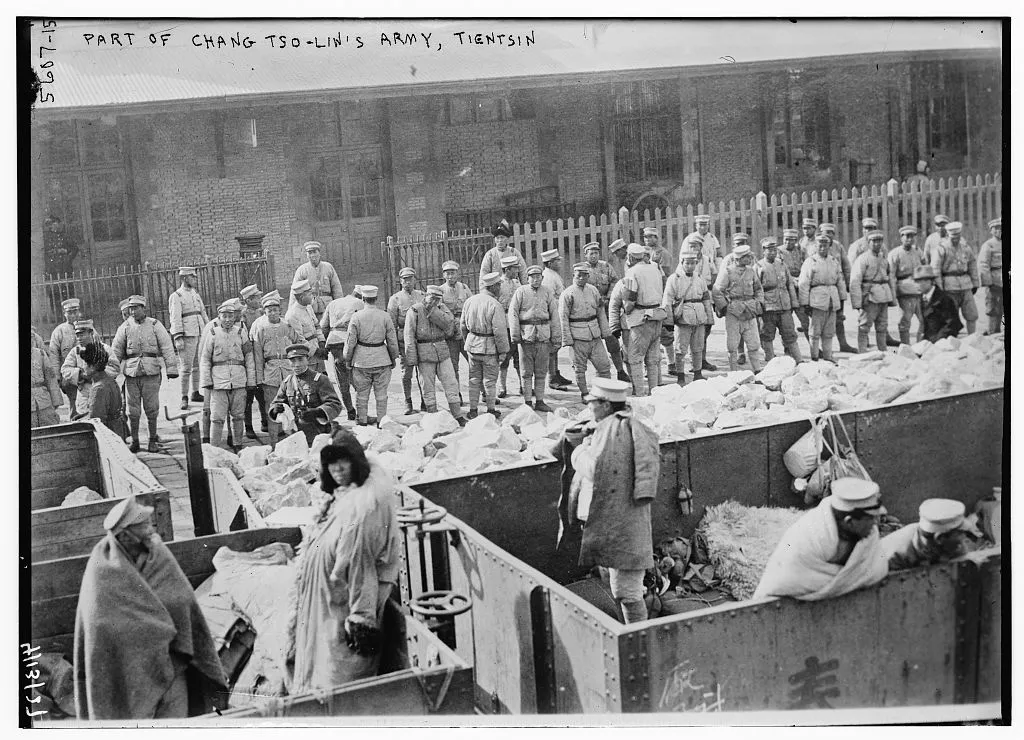 A black-and-white news photograph shows rows of Zhang Zuolin’s troops standing behind open freight wagons in Tianjin while workers and other figures occupy the foreground.